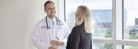 Dr. Brenner stands in front of a window talking to a patient.