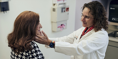 Dr. Virginia Kaklamani examines a patient's throat in an exam room.