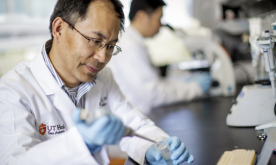 Mingjiang Xu, PhD holds a pipette, concentrating on a sample in a laboratory filled with scientific equipment.