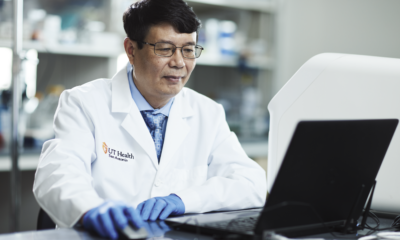 Daohong Zhou, MD researches in a white lab coat works at a laptop in a laboratory, focused and engaged in his task.