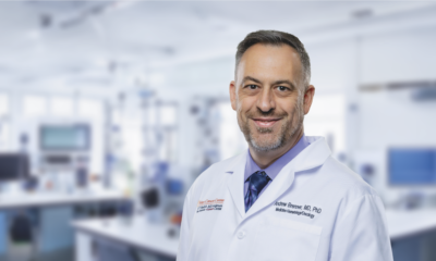 Andrew J. Brenner, MD, PhD smiles in a whitecoat in front of a lab.