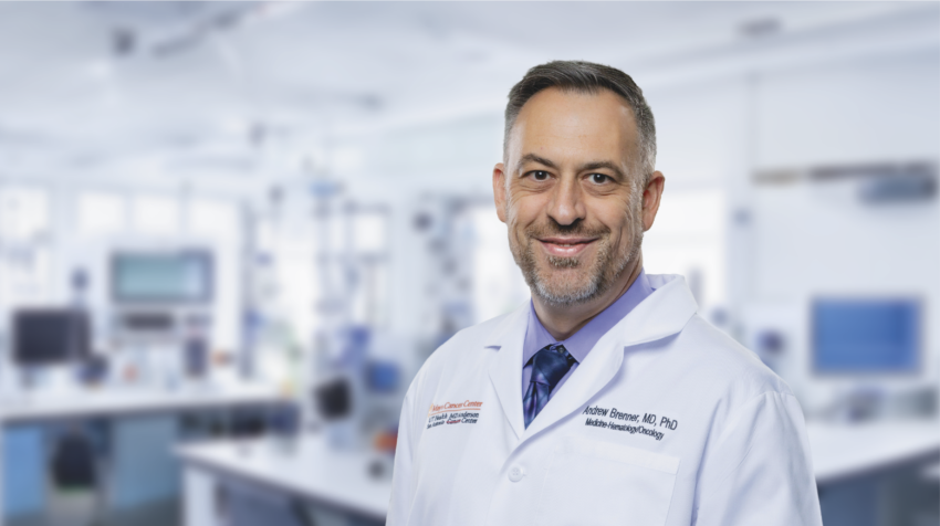 Andrew J. Brenner, MD, PhD smiles in a whitecoat in front of a lab.