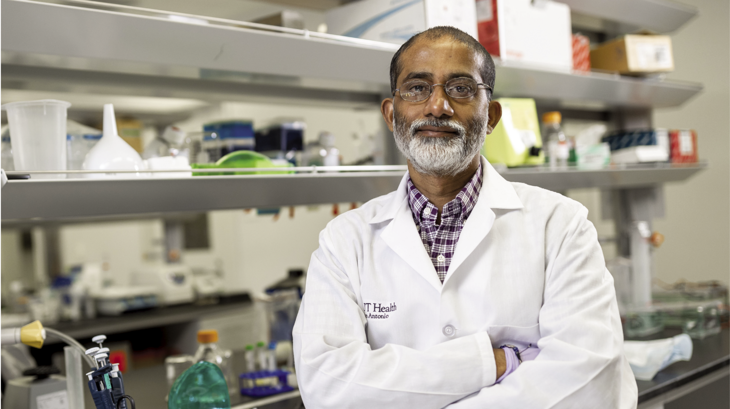 Sandeep Burma, PhD, stands in a lab in front of shelves filled with laboratory equipment. 