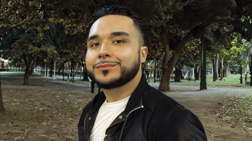 Angel Inocencio smiles while standing outside in front of some trees.