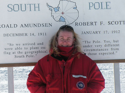 Desiree Dingman stands in front of the sign that designates the geographic South Pole.