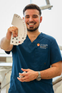 Wearing blue scrubs, Javy fans out a deck of cards in front of him while smiling.