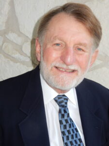 A head and shoulders photo of Dr. Benjamin Taylor in a black blazer and blue, checkered tie.