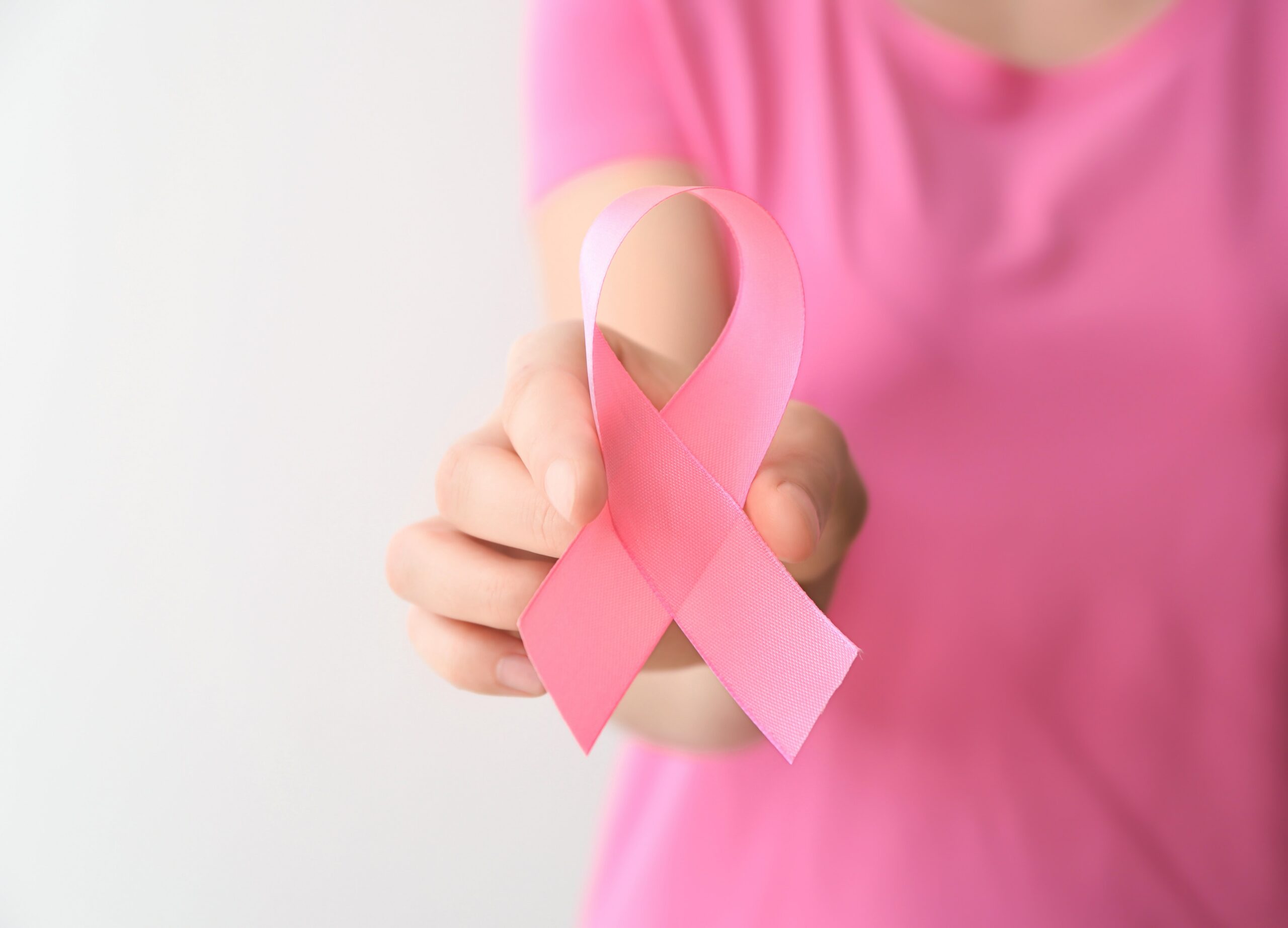 Woman holding pink ribbon on light background, closeup. Breast cancer awareness concept