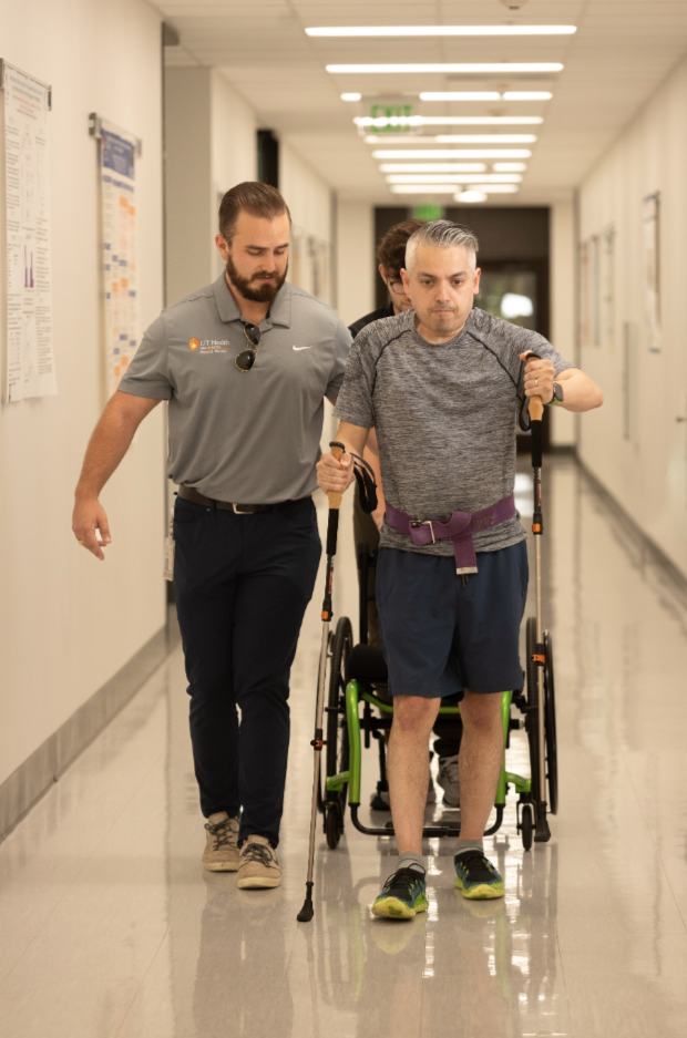 A patient walks with the aid of walking sticks supported by a health care professional.