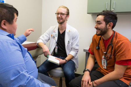 Medical student Nathaniel Nevitt (center) and B.S.N. student Matthew Gutierrez (right) visit with a patient at the Pride Community Clinic which serves the uninsured and underinsured lesbian, gay, bisexual, transgender and queer community.