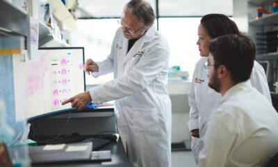 James D. Lechleiter, PhD, with Deborah Holstein, senior research associate, and doctoral graduate student Damian Lozano viewing a computer monitor in a lab.