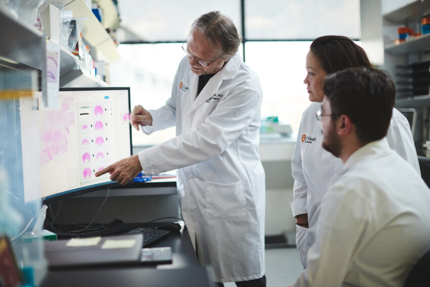 James D. Lechleiter, PhD, with Deborah Holstein, senior research associate, and doctoral graduate student Damian Lozano viewing a computer monitor in a lab.