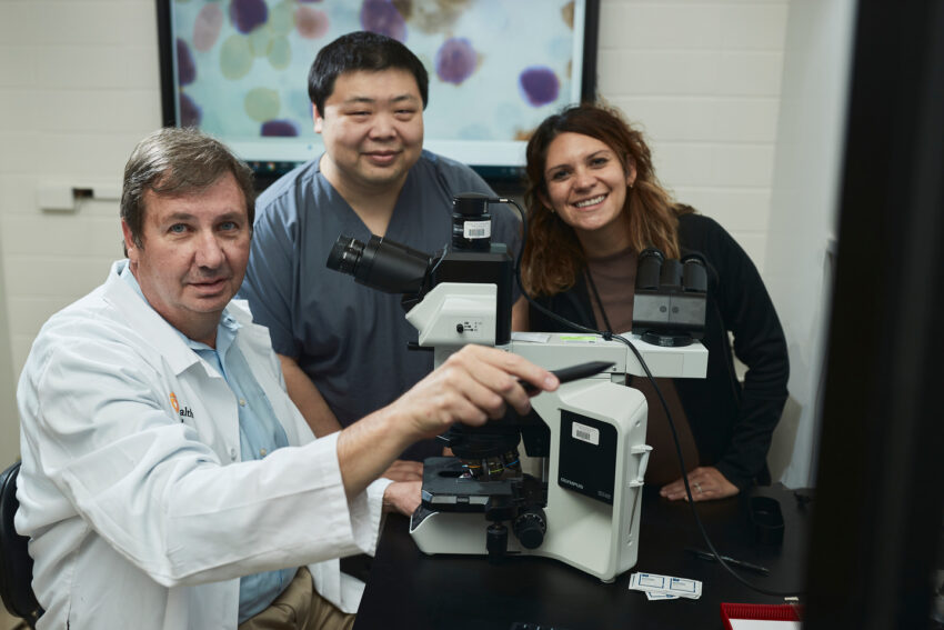 Bradley Brimhall, MD, with Yi Zhou, MD, clinical informatics fellow, and Ashley Windham, MD, MSDA, associate professor, around a microscope in Brimhall's lab.