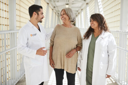 Two dentists in white coats stand beside a smiling patient in a beige top.