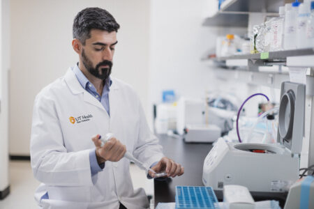 Researcher in a white lab coat dispenses a substance into a petri dish using a pipette.