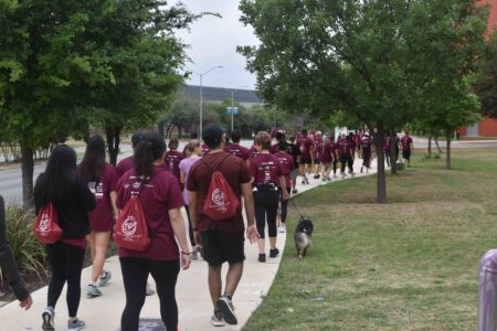 A group of event participants walk along the sidewalk wearing maroon event T-shirts and event backpacks.