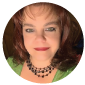 Woman with green eyes and red hair wearing a green top and black necklace smiles.
