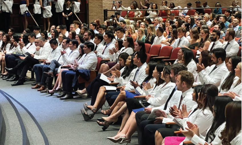 Dental students in their new white coast applauding in the auditorium.