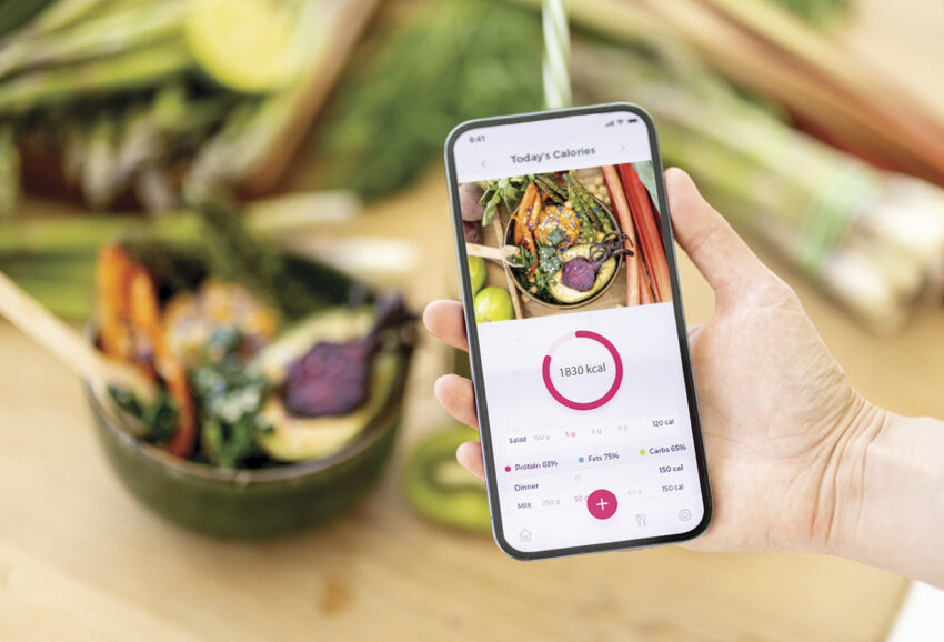 A person holds a phone with a health app open in front of a salad.