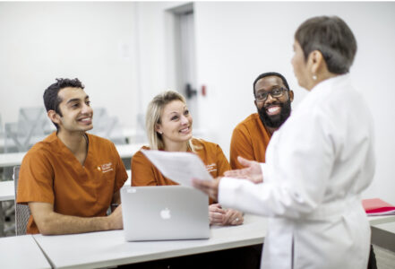 Three smiling nursing students talk to a professor.