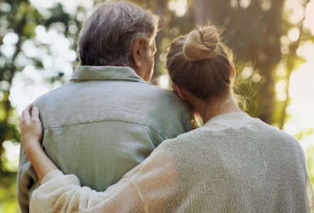 A daughter puts her arm around her father while they look into a sunset.