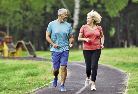Two older people walk side by side in a park.